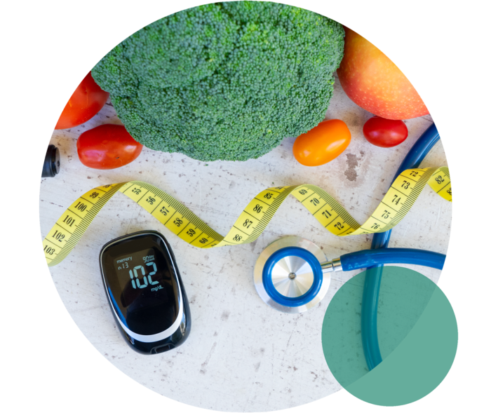 Ein Blutzuckermessgerät liegt neben einem Stethoskop, einem Maßband sowie Brokkoli, Tomaten und einem Apfel.