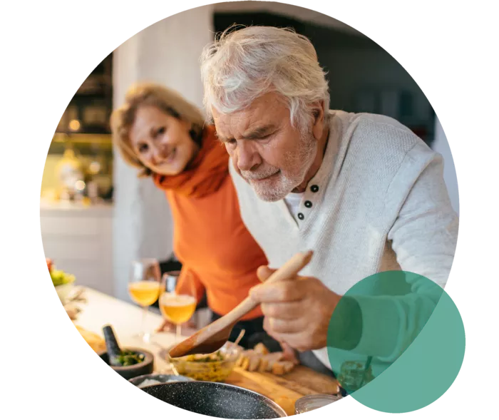Eine Frau und ein Mann im Seniorenalter an einem Herd. Sie neigen sich lächelnd über das kochende Essen.