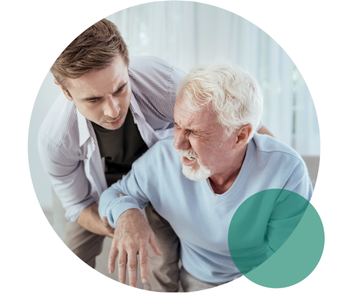 Senior mit schmerzverzerrtem Gesicht wird von einem jungen Mann gestützt.