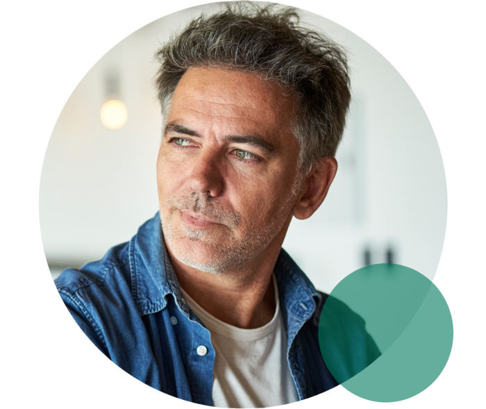 Mann mit ergrautem Haar und Dreitagebart blickt nach links.