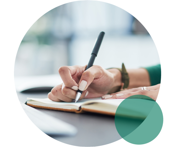 Hand hält einen Stift und notiert etwas in einem Notizbuch.