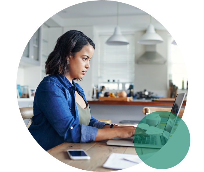 Junge Frau sitzt mit einem Notebook am Küchentisch und tippt etwas in die Tastatur.