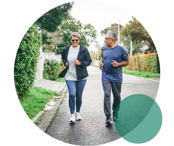 Eine Frau und ein Mann höheren Alters in Sportkleidung. Sie joggen gemeinsam auf einer Straße.