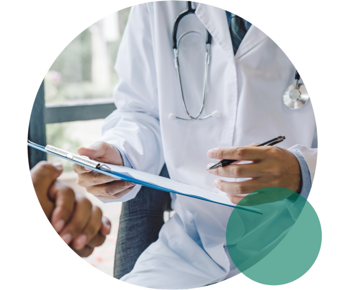 Hände und Oberkörper eines Mannes mit weißem Kittel. Er hält ein Klemmbrett und einen Stift. Gegenüber die gefalteten Hände einer weiteren Person.