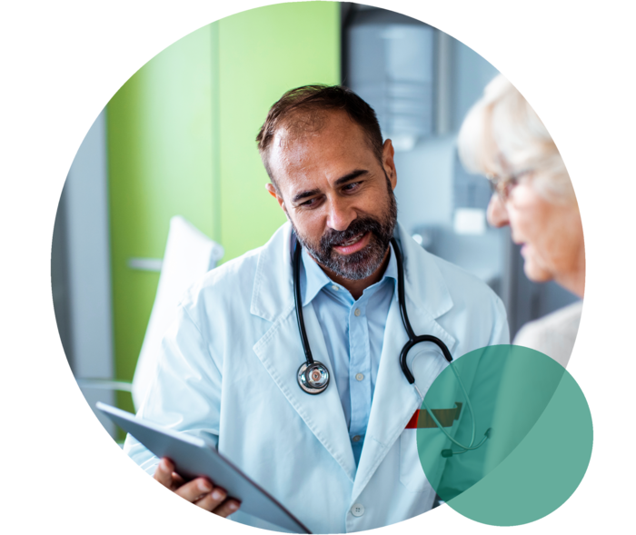 Ein Arzt und eine Patientin im Seniorenalter. Der Arzt hält ein Tablet, auf das beide blicken.