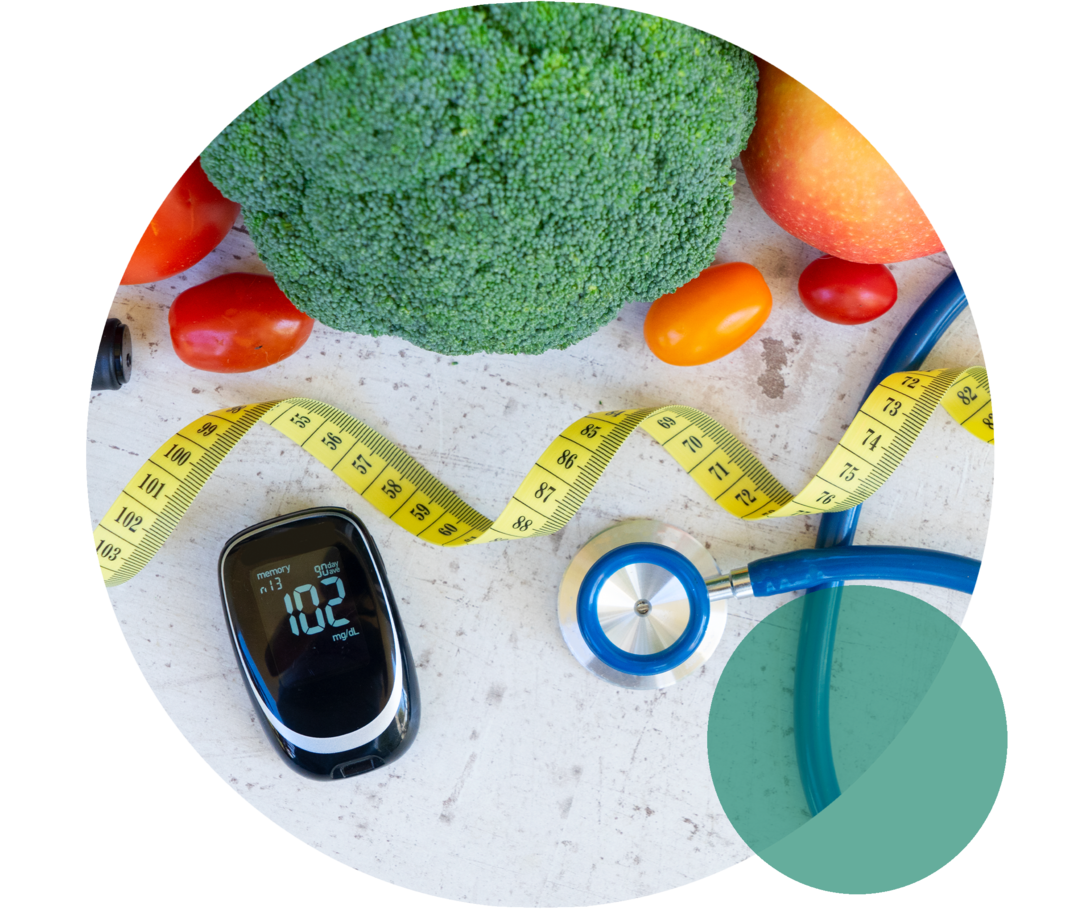 Ein Blutzuckermessgerät liegt neben einem Stethoskop, einem Maßband sowie Brokkoli, Tomaten und einem Apfel.