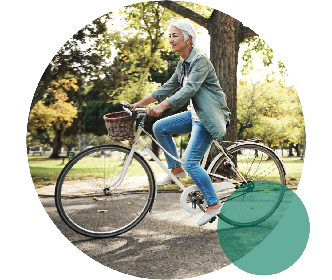 Eine Seniorin fährt in einem Park auf einem Fahrrad.