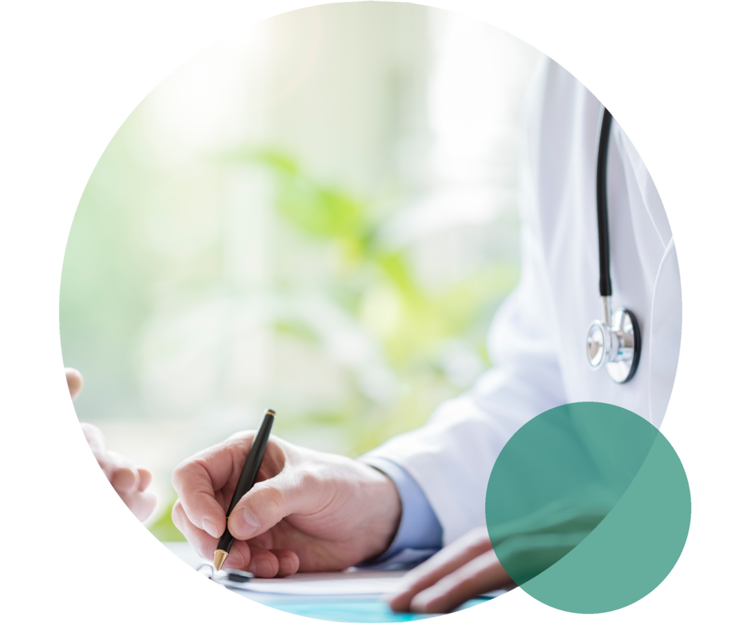 Person in weißem Kittel hält einen Stift und notiert etwas. Gegenüber sind die gefalteten Hände einer weiteren Person zu sehen.