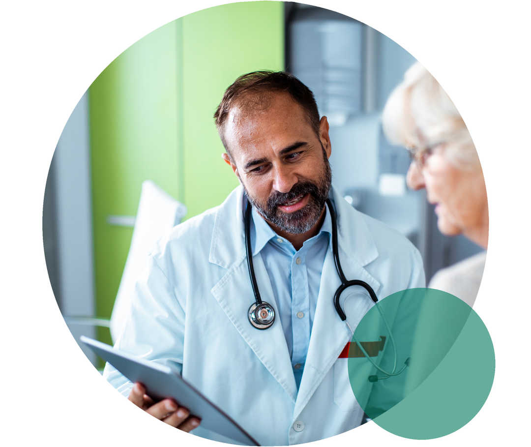 Ein Arzt und eine Patientin im Seniorenalter. Der Arzt hält ein Tablet, auf das beide blicken.