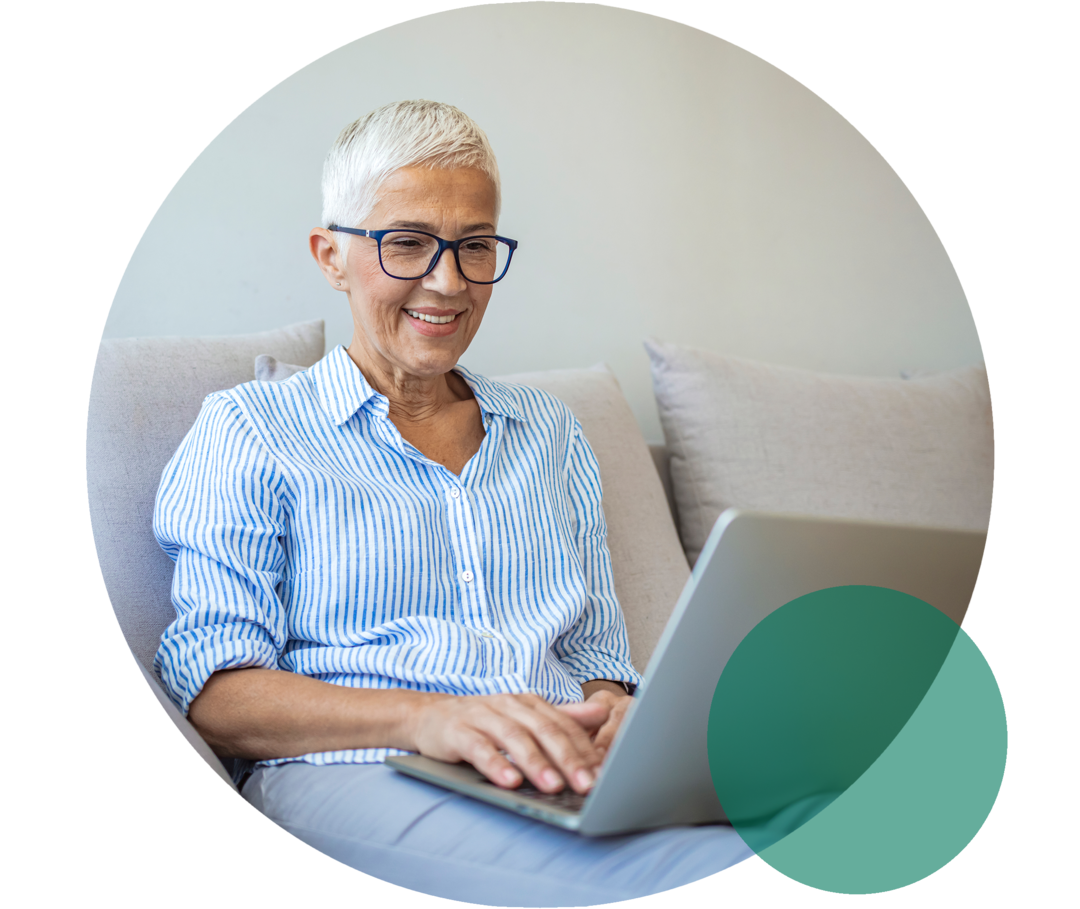 Digitales Magazin zur Herzgesundheit Seniorin sitzt lächelnd auf dem Sofa. Sie blickt auf den Bildschirm eines Laptops, der auf ihrem Schoß ruht.