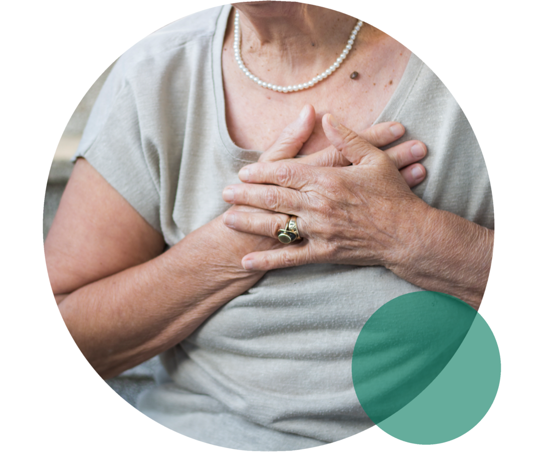 Oberkörper einer älteren Frau. Sie sitzt auf Treppenstufen und fasst sich mit beiden Händen an die Brust.